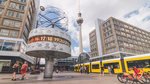 Urania-Weltzeituhr am Alexanderplatz in Berlin mit Fernsehturm und gelber Straßenbahn im Hintergrund.