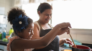 Young girl cooking with her mother.