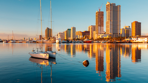  Skyline of Manila City and Manila Bay, Philippines. Skyscrapers and sailboats reflected in the water at sunset. 