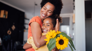 African American mother hugging her daughter and holding sunflowers.