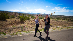 Two female pilgrims each carrying a wood cross walking along a highway in the desert  in northern New Mexico.