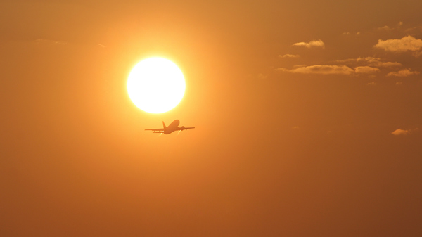 An airplane taking off with the rising Sun in the background.