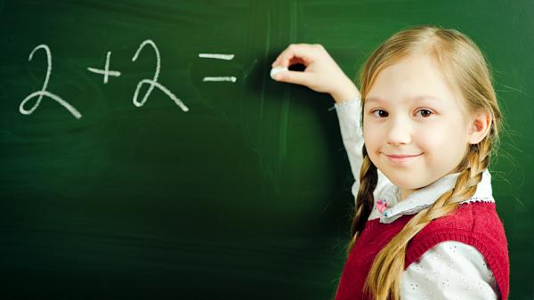 a young girl doing a simple calculation on a blackboard smiling at the fotographer.