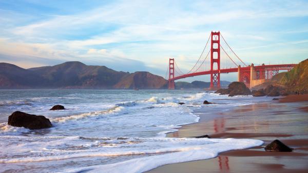 Beach with Golden Gate Bridge in background at sunset.