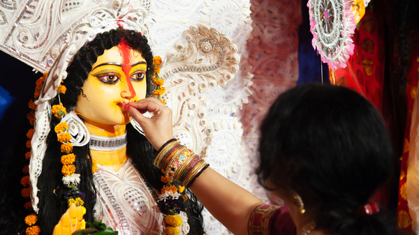 A woman in traditional Indian attire touches the mouth of a decorated idol of goddess Durga