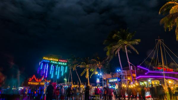 Partygoers on the beach at night amongst neon lights in Haad Rin, Ko Pha Ngan, Thailand.