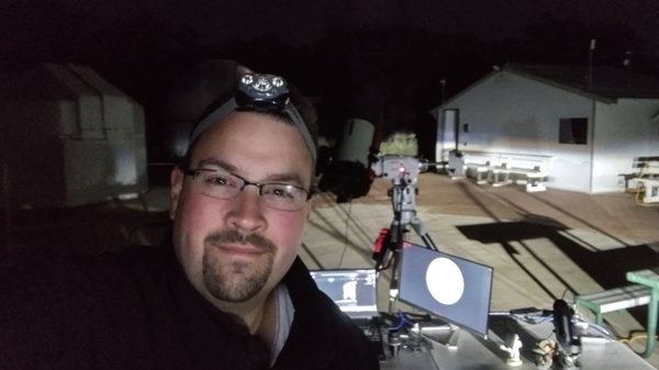 Man taking a selfie wearing headlamps at night. A computer and other equipment can be seen in the background.
