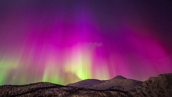 An image of vibrant pink, purple, and green aurora over mountains in Harstad, northern Norway.
