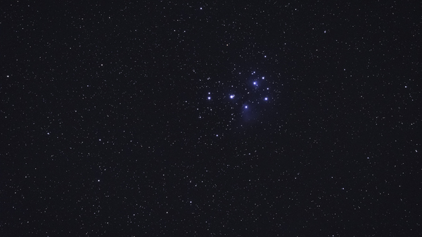 An image showing the Pleiades star cluster in a dark night sky.