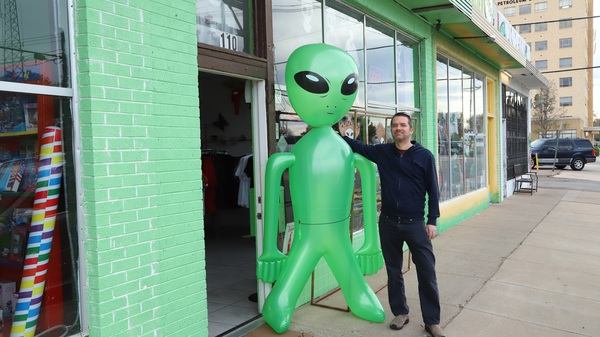 Man posing next to a large, green inflatable alien figure.