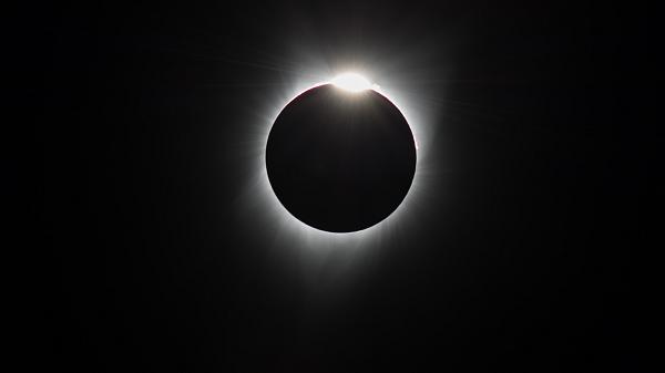 Black background with rays extending out from a circle and a bright light from the top of the circle.