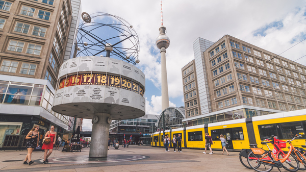 Urania-Weltzeituhr am Alexanderplatz in Berlin mit Fernsehturm und gelber Straßenbahn im Hintergrund.