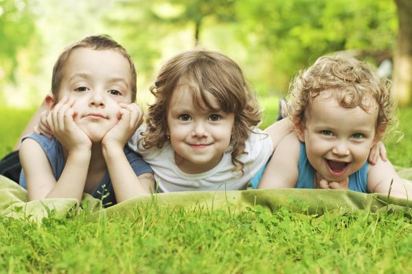 Three young children lying in the grass smiling. Three young children lying in the grass smiling.