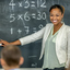 A smiling black woman pointing to a blackboard with math equations.