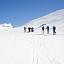 Sju personer sett bakfra går på ski i et snødekket landskap og med blå himmel.