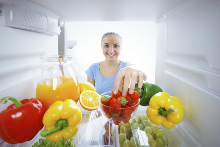 Woman reaching for strawberries in a fridge.