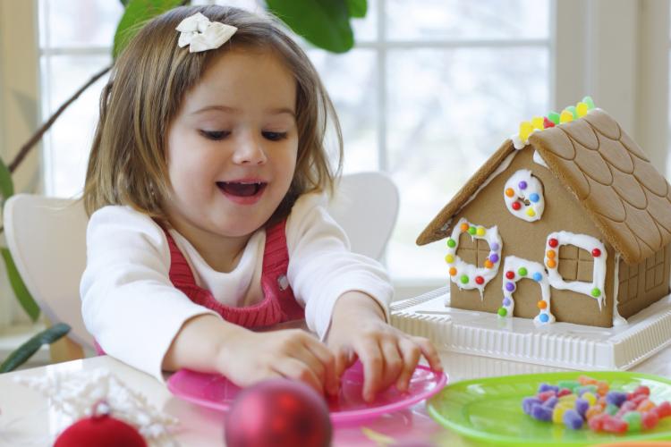 Little girl decorating a gingerbread house.