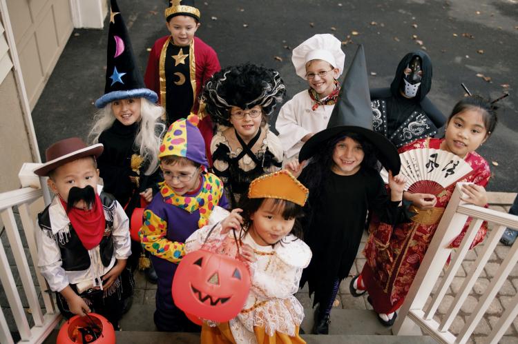 10 smiling kids in halloween costumes waiting for candy on a staircase while trick or treating 