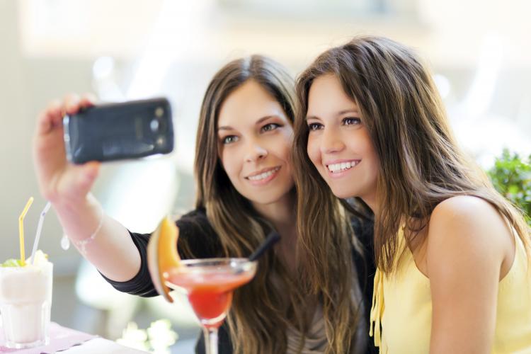 Two girls drinking cocktails and taking a selfie outdoors.