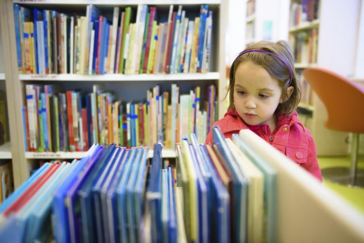 Little girl choosing a book in the library.