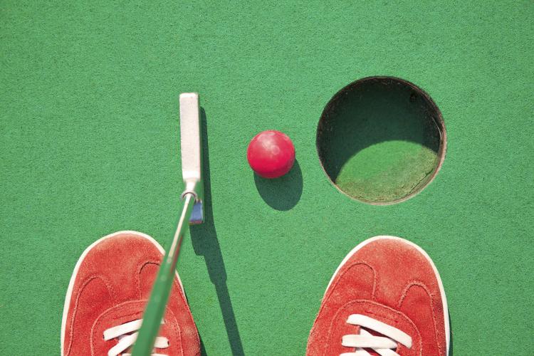 Miniature golf, red shoes and ball near a putting hole.