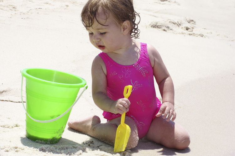 Baby with a bucket on the beach.