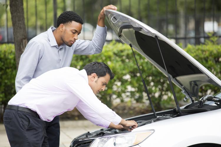 Man helping another man to look at car engine.