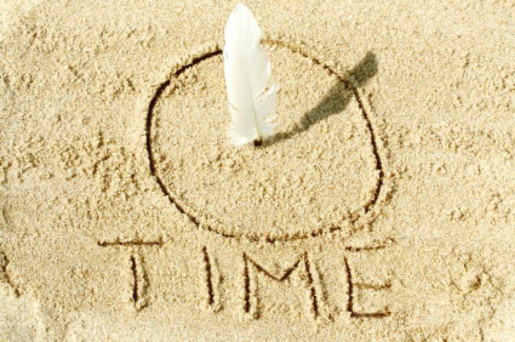 Sundial on the sand with a white feather