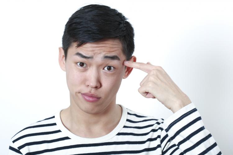 Young Asian man pointing index finger against his temple. Click to see more detail. Young Asian man pointing index finger against his temple.