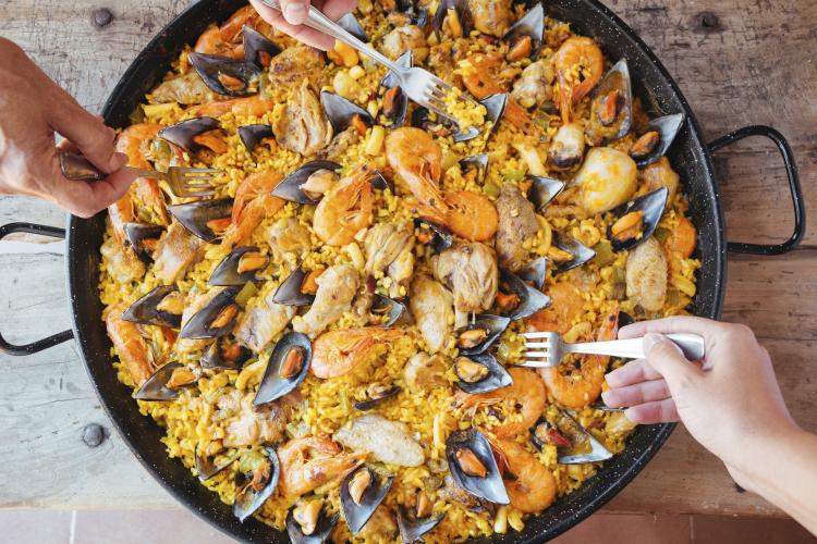 A big pan of mixed paella and forks taking bites from it.
