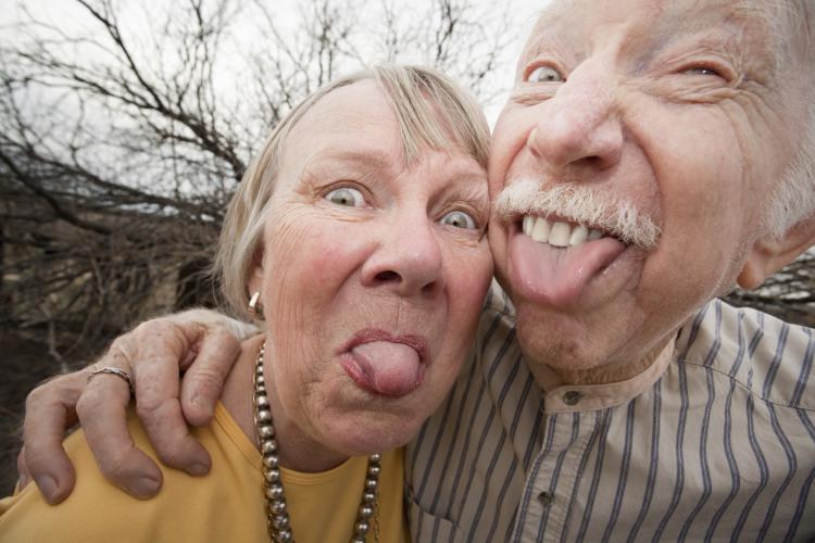 Closeup portrait of an elderly couple outdoors sticking out tongues.