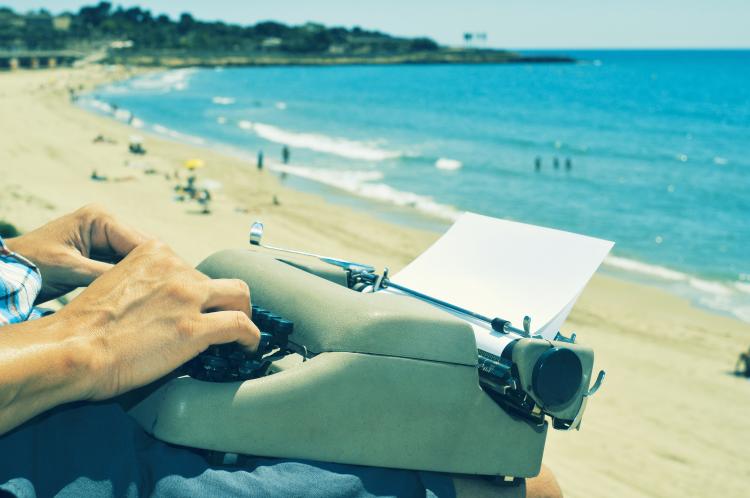 A young man typing on an old typewriter at the beach.