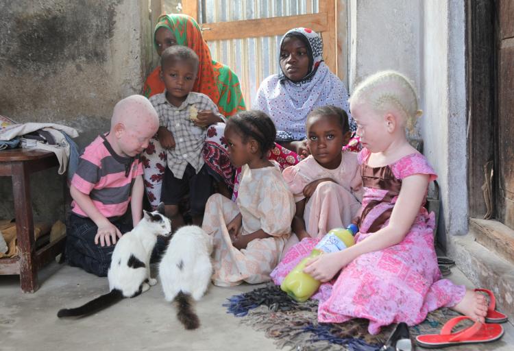 Tanzanian family seated on the floor of their house showing two women and five children, including a son and a daughter with Albinism.