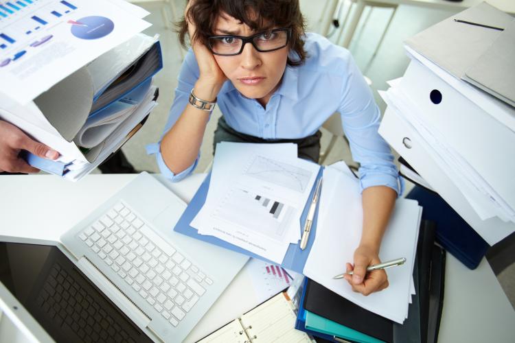 An accountant doing financial reports while surrounded by huge piles of documents.