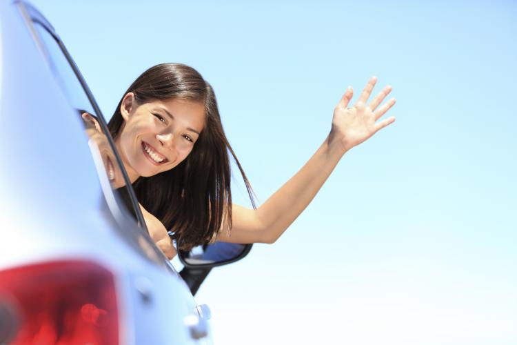 Woman waving hello out of a car window.