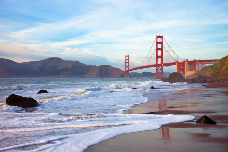 Beach with Golden Gate Bridge in background at sunset.