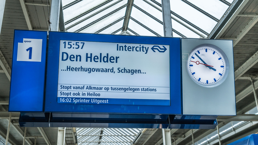 A blue and white display showing information about a train departure in Dutch, with an analog clock next to it.