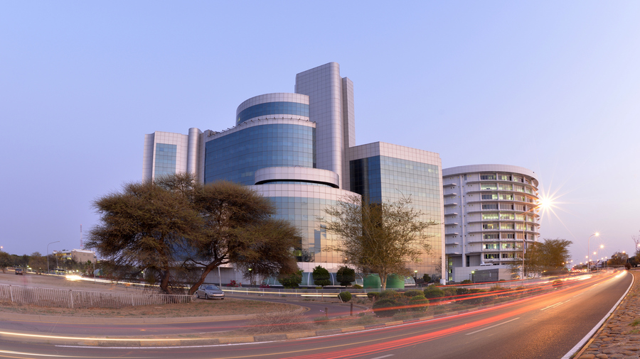 The attorney general chambers building in Gaborone, Botswana, photographed with longer exposure in the evening hours, showing streaking lights of cars in front of a glass and metal office building.