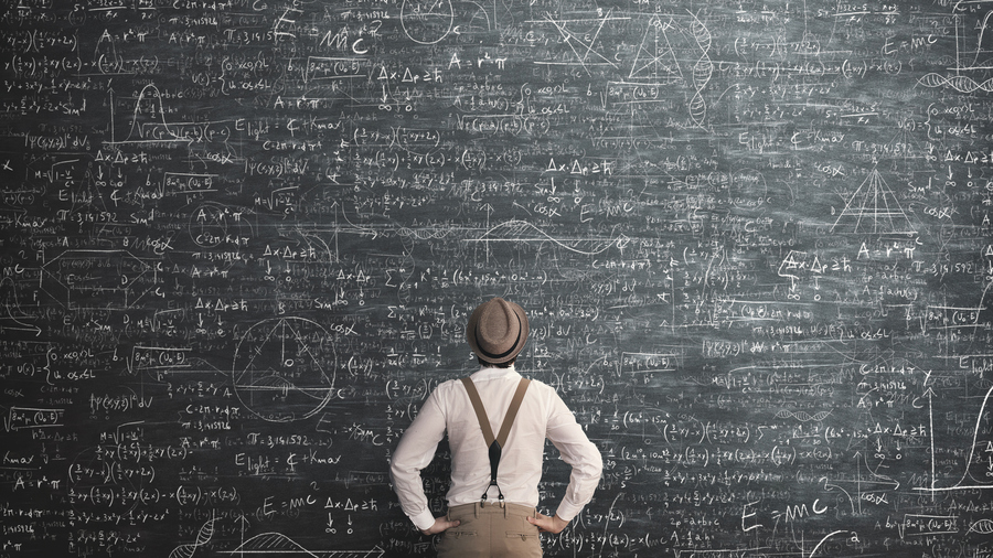 A man standing in front of a very large blackboard with math equations scribbled all over it.
