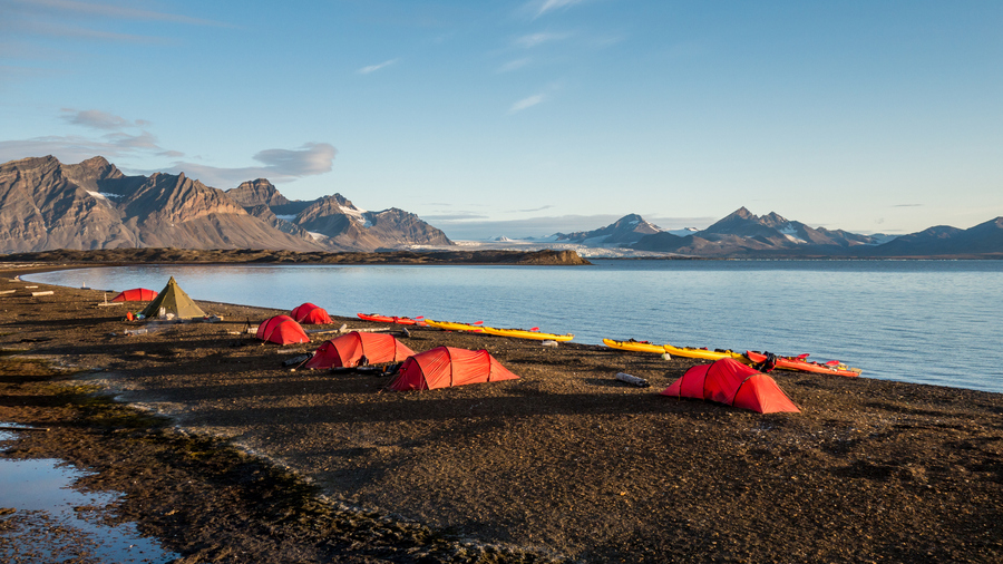 Colorful tents at a remote campsite in Svalbard under the midnight sun, surrounded by Arctic mountains and snow patches.