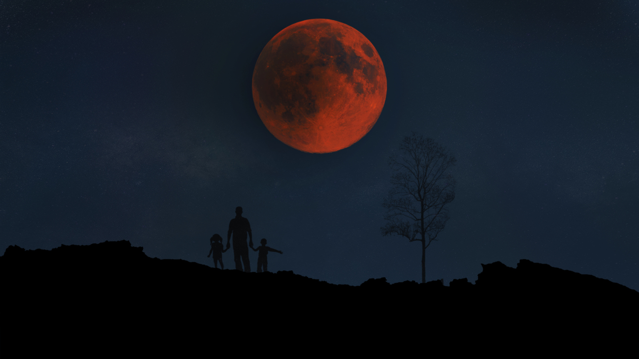 Silhouettes of a person and two children standing on a hill against a dark night sky, with a large, red-hued fully eclipsed moon above them. 