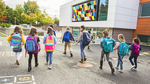 En gruppe barn som går i sammen ved en moderne skole med fargerike skolesekker.