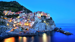Italienisches Dorf Mararola in Cinque Terre bei Dämmerung; hell bereuchtete Häuser an einem Hang über dem Meer.