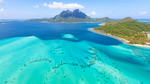Luftbild der Südseeinsel Bora Bora mit blauem Meer, Sandstrand und bewaldeten Inseln.