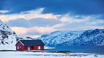 Rød hytte ved sjøen i snødekt landskap.