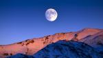 Moon rising over snowy mountains.