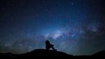 A man's silhouette with the milky way and a meteor in the backdrop.