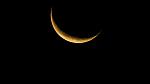 A close-up of the thin sliver of a yellow waning crescent moon.