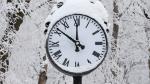 Clock with snow on it during the winter time.