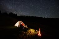 Couple sitting outside their camp in the mountains under a starry night sky.
